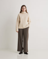 Woman wearing a beige sweater and brown pants on a white background